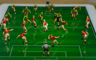 Side view of miniature toys figurines football (soccer) players on a computer electronic pad.