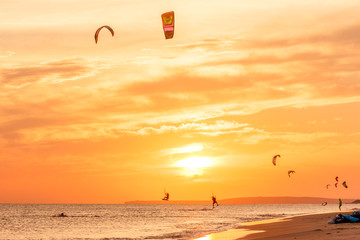 extreme group of professional kiters slide waves, jumps air on black sea with sail wing in hands led wind an sunset, onlookers photographers seagull on shore. village of annunciation. backlit, toned