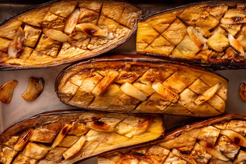 A closeup of roasted eggplants with garlic, shot from the top in a baking tray