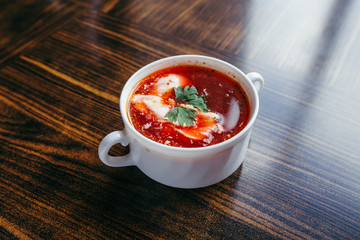 Christmas beetroot soup, borscht with small dumplings with mushroom filling in a ceramic bowl on a wooden table.