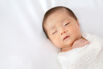Sleeping newborn baby in white wrap while on white blanket background.