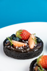 Cookie crust chocolate tart with Blueberry and strawberry set on Blue Background.