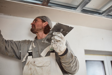 Workman plastering gypsum walls inside the house.