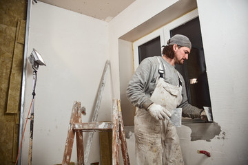 Workman plastering gypsum walls inside the house.