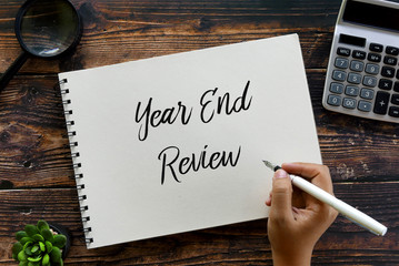 Top view of magnifying glass,calculator,plant,pen and hand writing ' Year End Review ' on a notebook on wooden background.