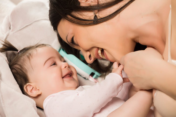 A happy young mom plays with her baby daughter on a white background