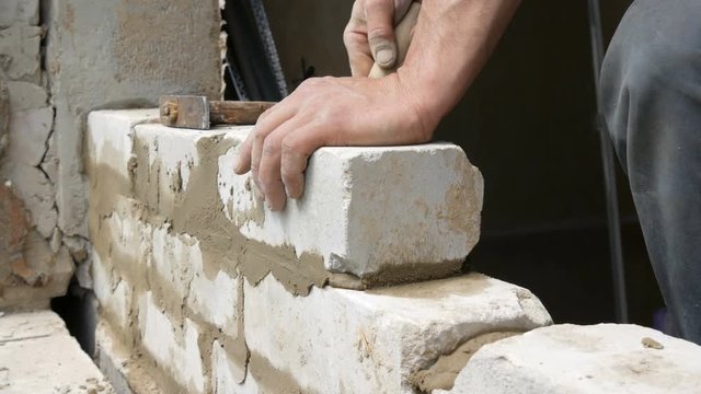 Male builder laying white brick on cement and standing wall. Hands of a man laying building bricks close up view