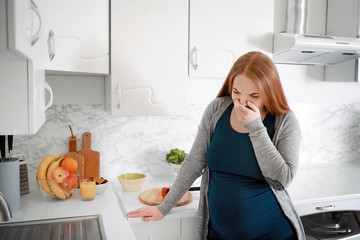 Young pregnant woman suffering from toxicosis in kitchen