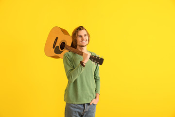 Handsome young man with guitar on color background