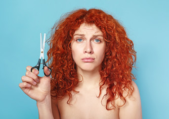 Fototapeta premium Beautiful woman displeased with her hair holding scissors on color background