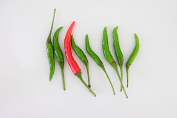 one red chilli among green chillies on white background
