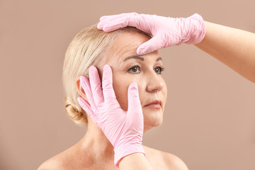 Plastic surgeon touching face of mature woman on color background
