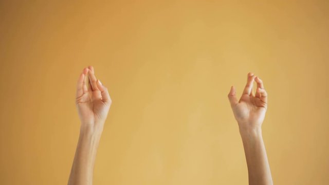 Close-up shot of female hands making praying gestures crossing fingers putting palms together in namaste on orange background. Body language and feelings concept.