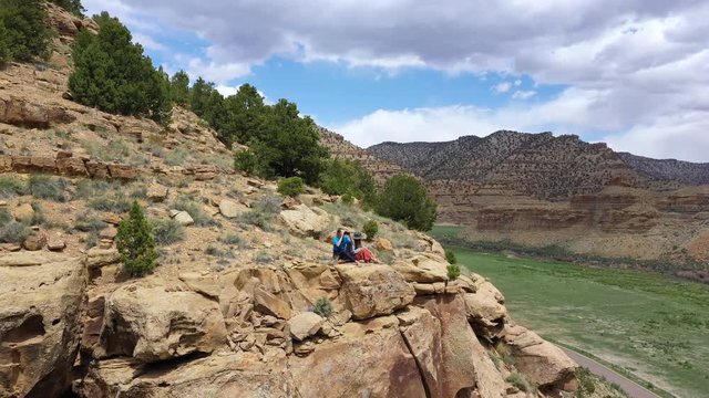 Two women sitting on edge of cliff looking over the valley while rotating around them in the Utah desert.
