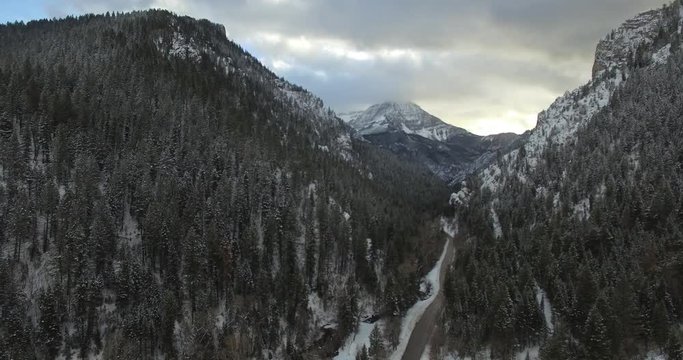 aerial shot of man and woman standing at edge of cliff, drone passes over them towards snow covered mountains