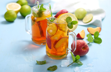 Iced tea with peaches, lemons, limes and mint with ice cubes, summer refreshment drink