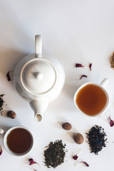 Tea set with white ceramic tea pot, dried rose flowers and other tea ingredients on the white. Flat lay view of various dried teas and teapot. View from above. Space for your text