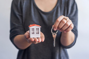 Woman holding miniature toy house and keys. Real estate agent holding keys and toy house. Buying or selling real estate