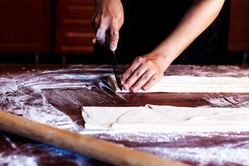Young house wife preparing the homemade pasta at kitchen. Woman cutting long dough stripe for cooking pasta.