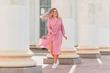 Happy woman of plus size, American or European appearance walks in the city enjoying life. Young lady with excess weight, stylishly dressed at the city park .Natural beauty