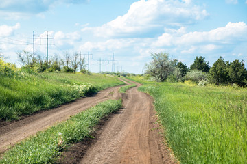 Fototapeta na wymiar rural road between field and small forest, blue sky with clouds