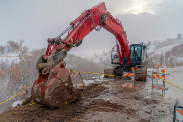 Excavator on a muddy road with barricades and yellow tape viewed in winter