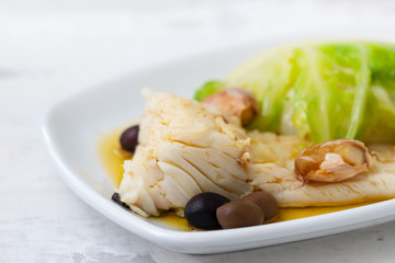 boiled cod fish with olive oil and vegetables on white plate