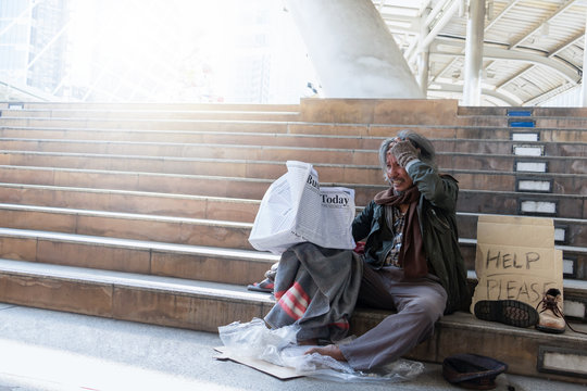 Homeless man is sitting down on staircase in town.He is read newspaper.He is very unhappy. poverty,despair, Photo Sympathetic and hope concept.