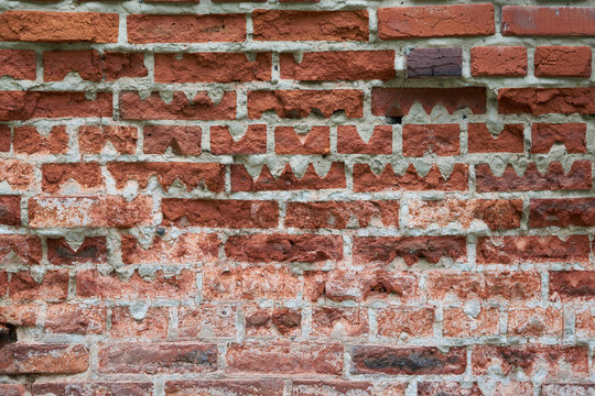 Old red brick wall of rectangular shape with triangular cutouts. Pieces of bricks partially broke off and cracked. Some bricks are of non-standard shape with cutouts of wavy shape.