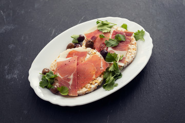 crispy rice diet toasts with prosciutto on ceramic background