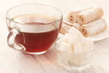 Hot tea with sugar cubes and sweets on table
