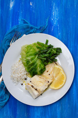 boiled cod fish with rice and vegetables on white plate