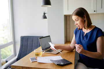 Stressed over bills. Portrait of surprised young woman using a laptop computer sitting at her...