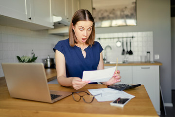 Stressed over bills. Portrait of surprised young woman using a laptop computer sitting at her...