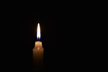 Candle burning in the black background. Located on the left side of the shot.