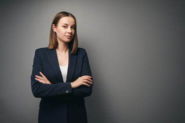 Confident young business woman in suit looking at camera. Grey background with copy space.