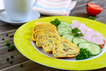 Omelette, egg roll with ham and fresh cucumber on a wooden table. Tasty healthy breakfast.