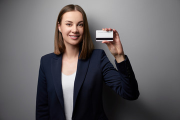 Pretty young business woman showing plastic credit card. Grey background.