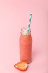 sweet and tasty smoothie in glass bottle with straw near red strawberry on pink