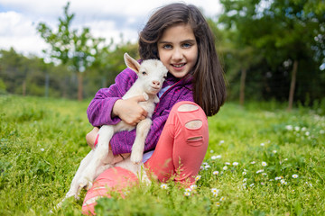 Little girl hugging a goat  on a field