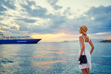 Traveling by Greece. Young happy woman enjoying beautiful sunset on the sea wharf waiting for ferry.