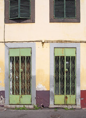 rusting green metal doors with ornate lattice work on the front of a derelict abandoned shop with faded yellow and red walls and shutters in funchal madeira