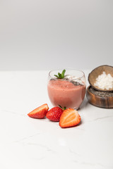 tasty smoothie with coconut flakes in glass near tasty strawberries on grey