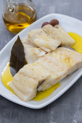boiled cod fish with olive oil on white dish on ceramic background