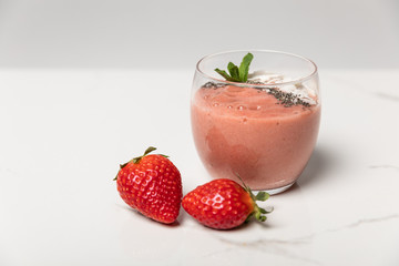 sweet ripe strawberries near tasty smoothie in glass on white