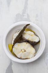 boiled fish with olive oil in white bowl on ceramic background