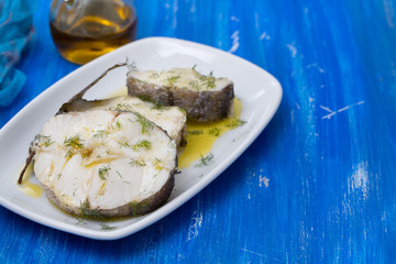boiled fish with olive oil in white dish on blue wooden background