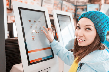 Happy Asian woman orders food in the touch screen terminal with electronic menu in fastfood restaurant. Modern technology concept