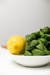 selective focus of fresh spinach leaves near yellow ripe lemon on grey