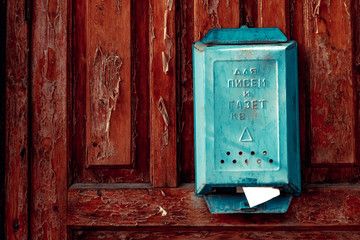 a turquoise vintage mailbox hangs on the weather-shattered door with shabby red paint; the inscription on the mailbox "For letters and newspapers"